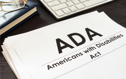 Stack of papers with Americans with Disabilities Act printed on the top page a book with a pair of glasses, and computer keyboard.