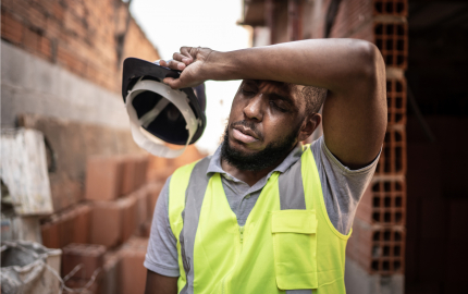 Man holding a hard hat using his forearm to wipe his forehead.
