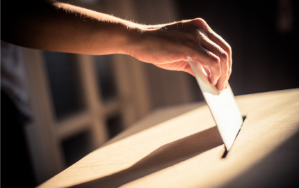 hand placing a folded piece of paper in a slit cut in the top of a wooden box.