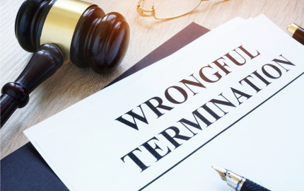 A gavel, pair of glasses, paper with wrongful termination printed at the top of the paper, and an uncapped pen.